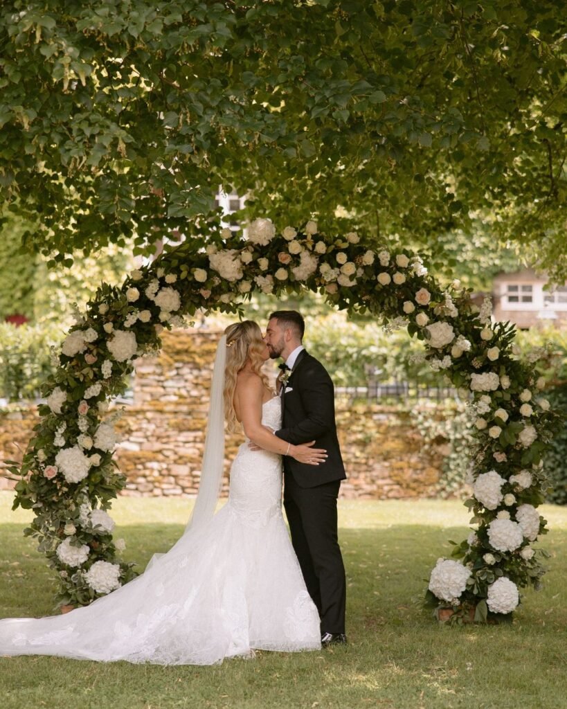 The couple exchanges vows under a romantic floral arch at Domaine d'Essendieras, with lush greenery and soft blooms framing the moment.