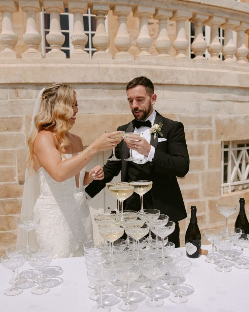 The couple pours champagne into a tower of glasses, a glamorous and celebratory moment at Domaine d'Essendieras.