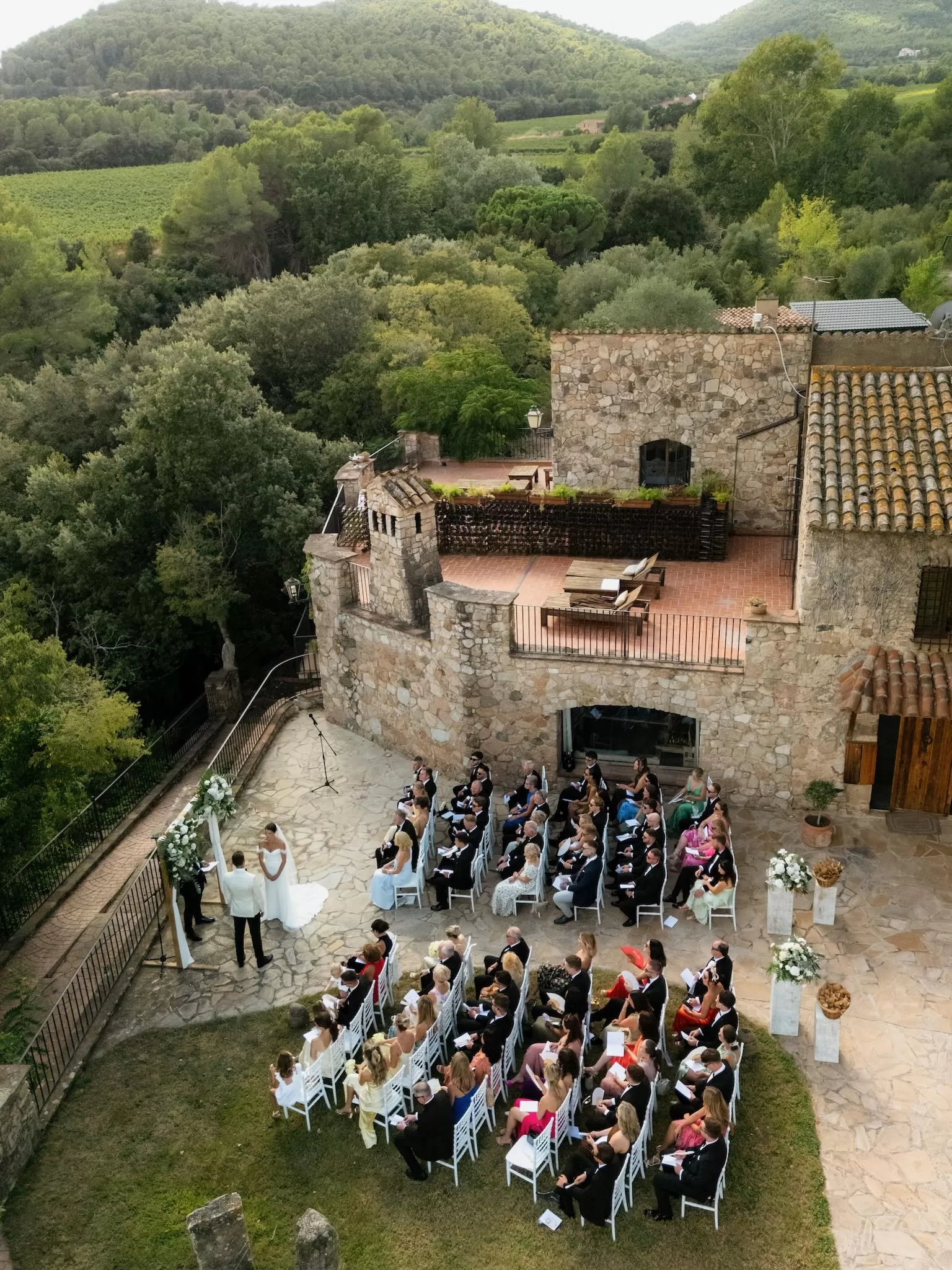 Aerial shot of the ceremony at Mas del Sord with guests seated around the stone terrace and lush hillside views.