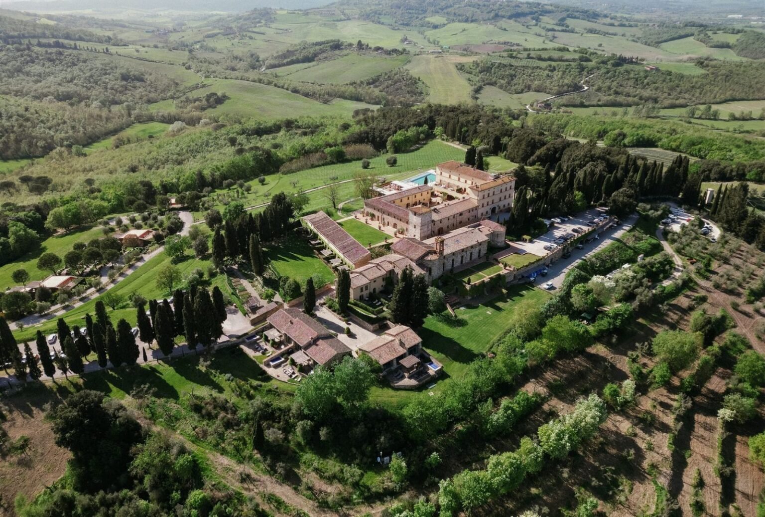 A wide aerial shot showcasing the historic estate of Rosewood Castiglion del Bosco, nestled in the Tuscan countryside.