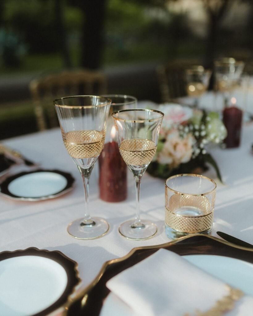 Elegant gold-rimmed glassware set on a white linen table for the wedding reception at Villa Ivana.