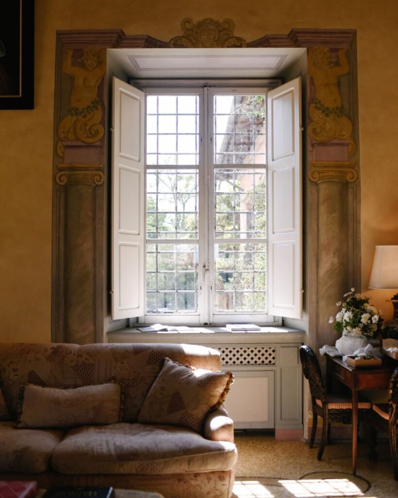 Sunlit historic window framed by ornate architecture inside Villa Mangiacane, illuminating a cozy sitting area
