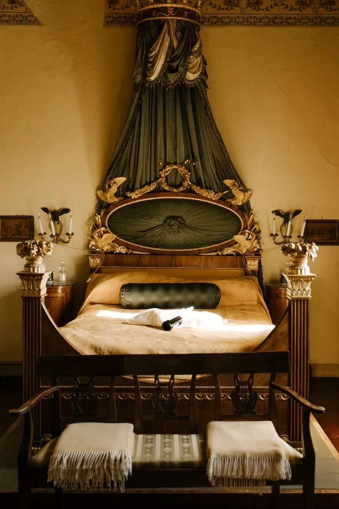 Regal four-poster bed with ornate canopy in a romantic suite at Borgo Stomennano, bathed in soft golden light.