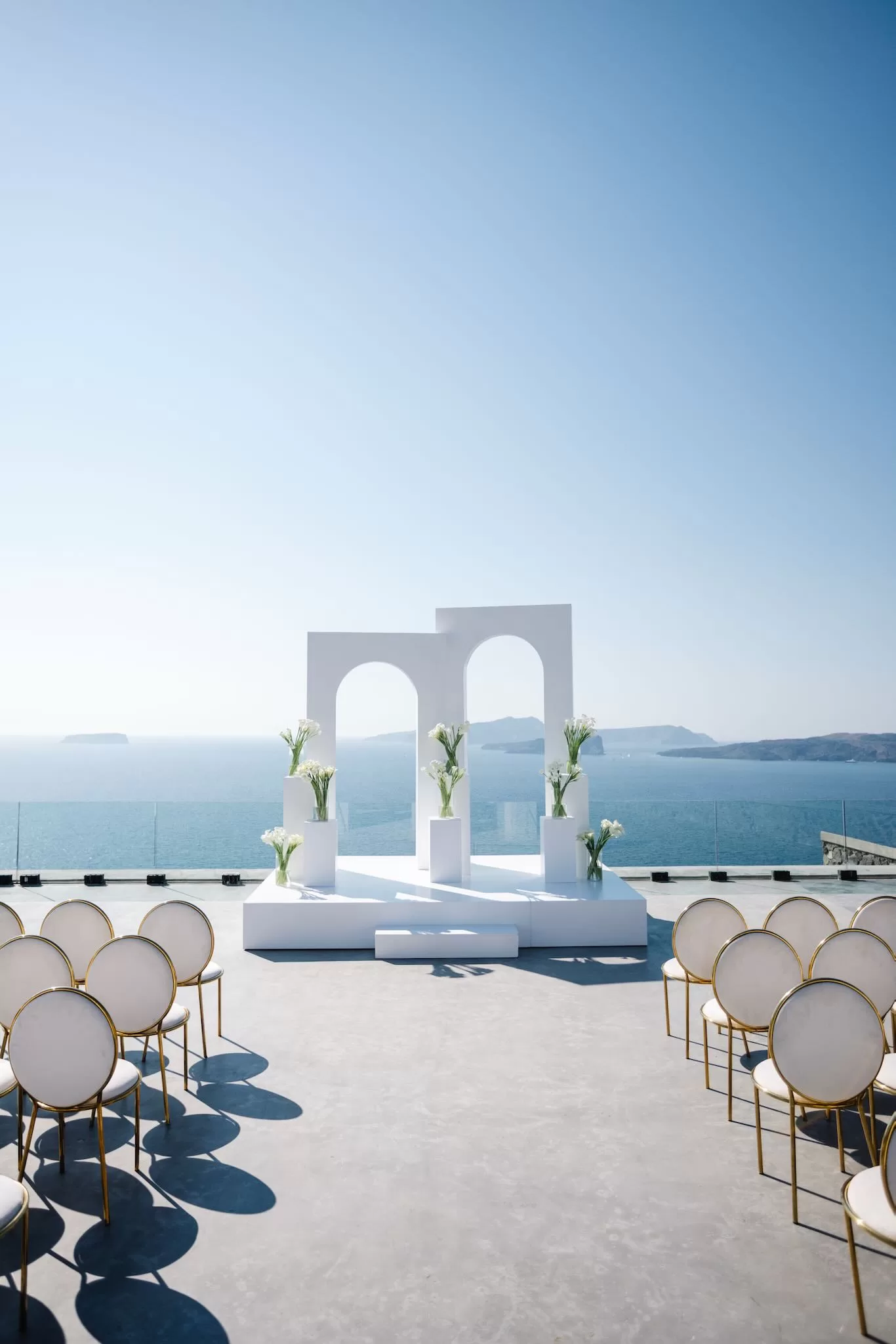 Wedding ceremony setup at Cavo Ventus with white arches and seating arranged to face panoramic Aegean Sea views.