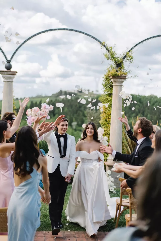 The newlyweds celebrating their ceremony exit under falling petals at Tenuta Corbinaia, surrounded by friends and scenic Tuscan hills