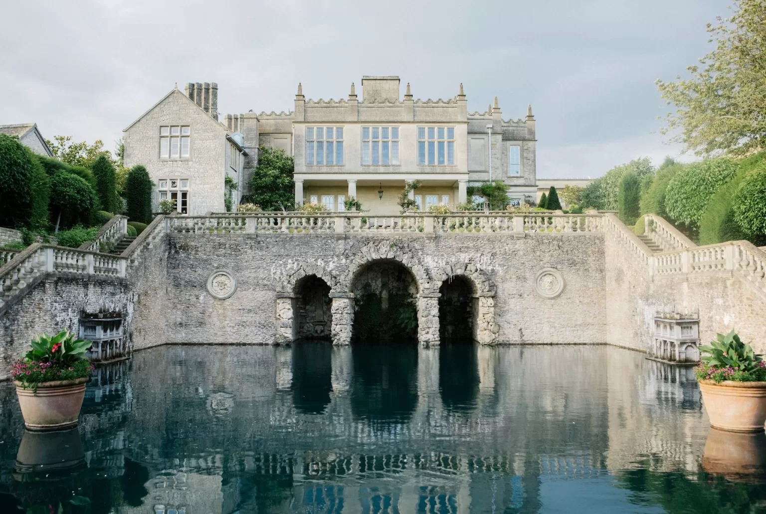 The grand facade of Euridge Manor reflected in the tranquil pool below, framed by symmetrical staircases and potted plants.