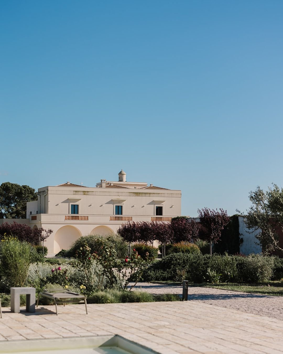 Grand entrance to Masseria Fontana di Vite, framed by lush greenery and bathed in warm Mediterranean sunlight.