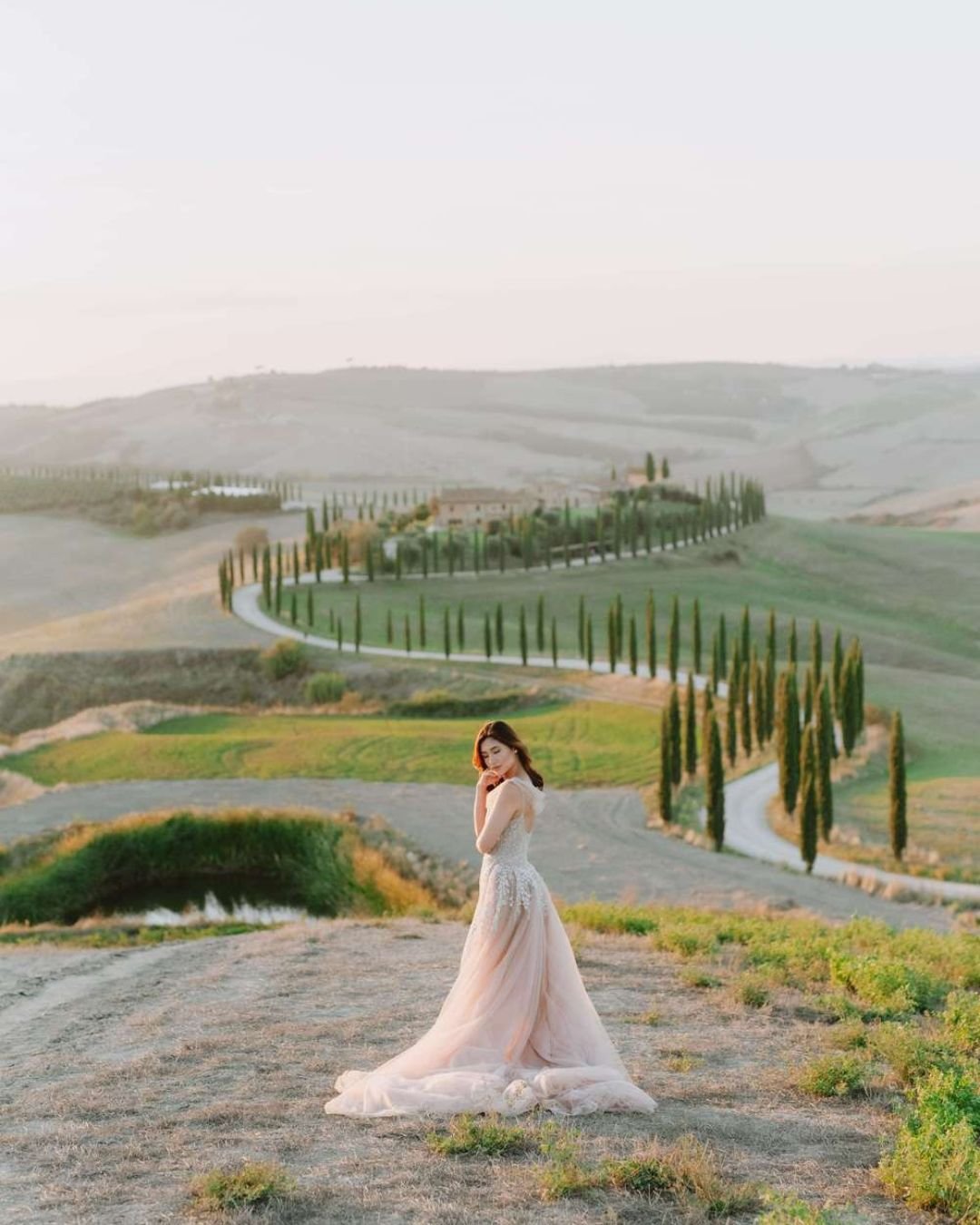 Bride gazing out of a window, bathed in soft, dreamy natural light.