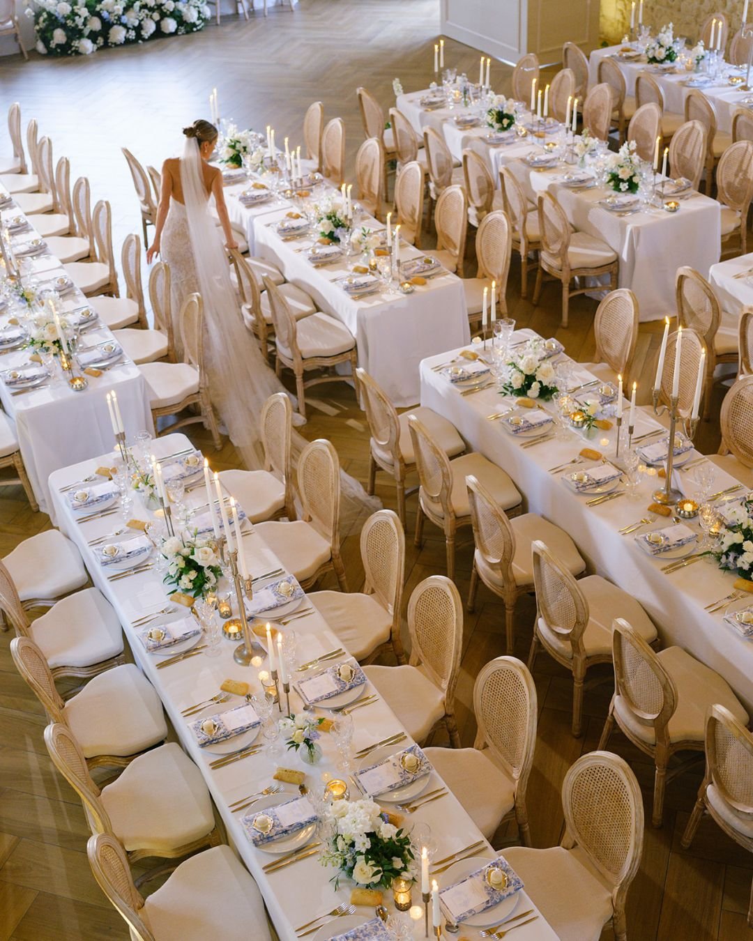 Elegant rows of reception tables adorned with candles and floral arrangements for a romantic wedding dinner.
