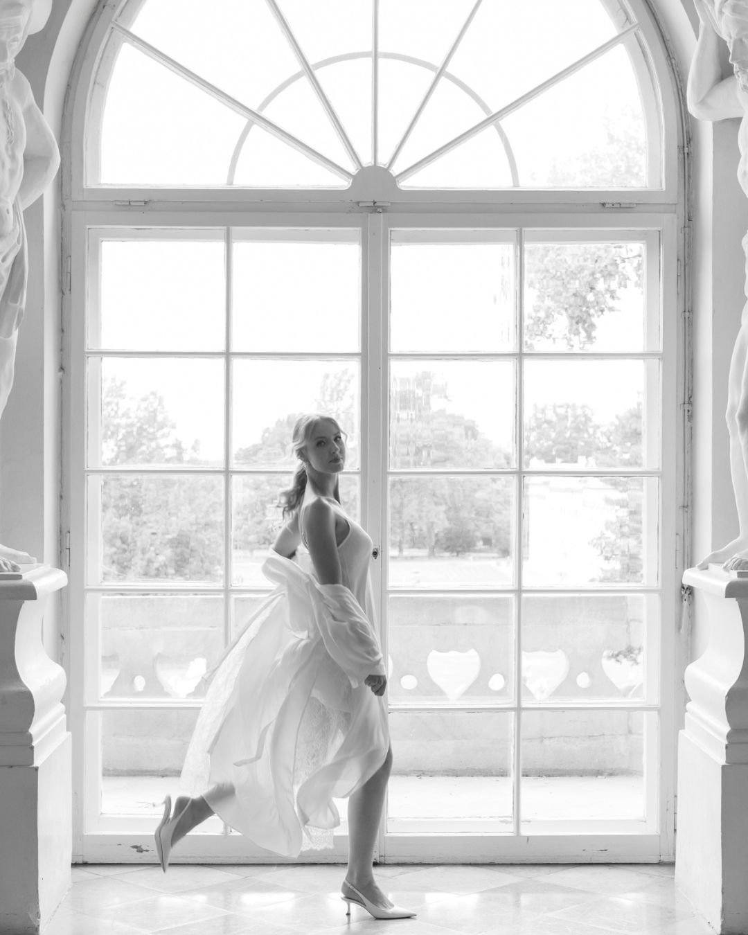 Artistic black-and-white bridal portrait near large, arched window, taken by Sylwia Zylka.