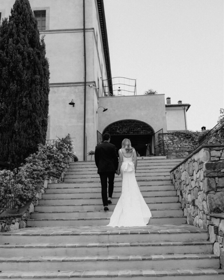 The couple walks up the grand stone staircase of Rosewood Castiglion del Bosco, the bride’s dress flowing behind her.