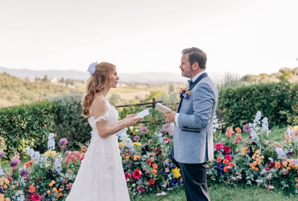 The couple stands at the altar during their wedding ceremony, with rolling Tuscan hills stretching behind them.