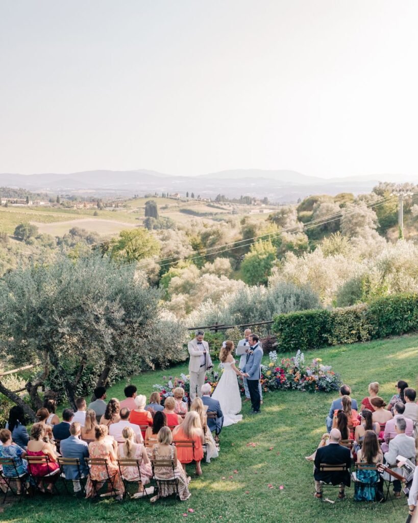 A breathtaking wide-angle view of the ceremony setup at Quercia al Poggio, framed by vineyards and olive trees.