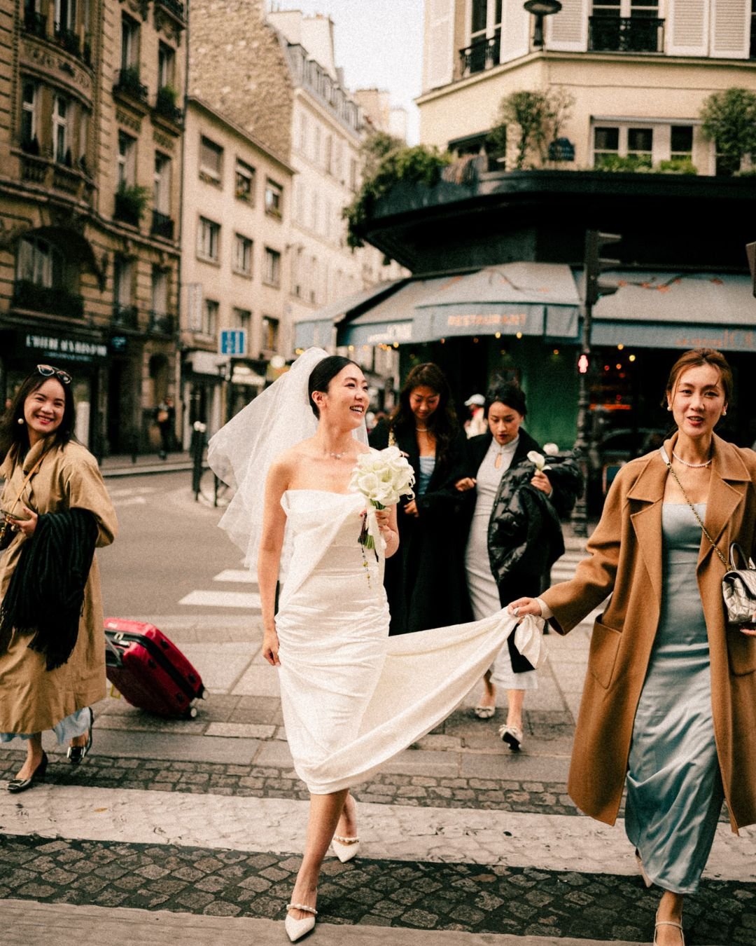 A stylish bride and groom crossing the street in a bustling cityscape.