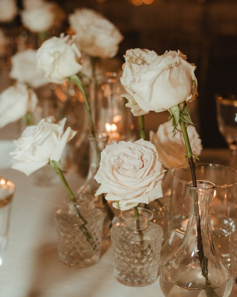 Soft white roses in minimalist vases adorn the reception tables at Villa Donna Camilla’s wedding celebration.