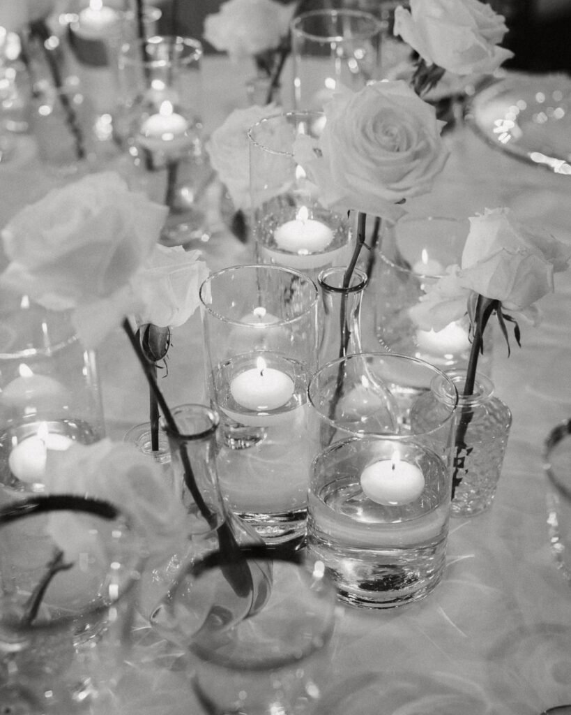 Soft candlelight reflects off glass vases filled with delicate white flowers at Villa Donna Camilla’s reception tables.