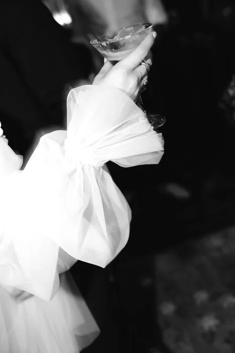 Bride toasting with a martini glass, wearing a dramatic tulle sleeve during a chic wedding celebration at Borgo Stomennano.