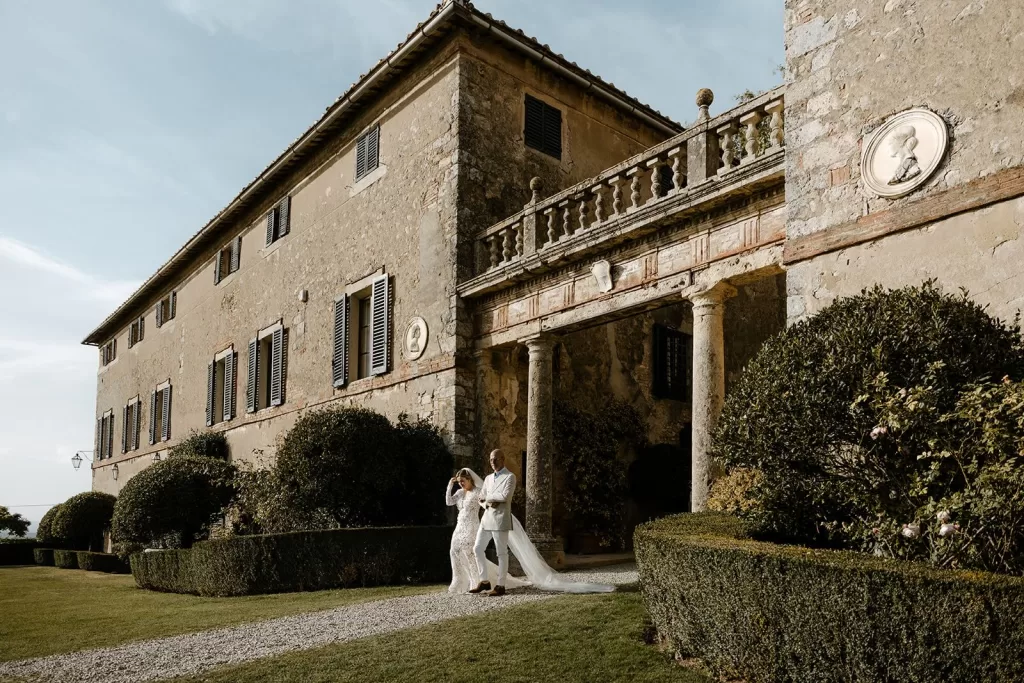 Bride and groom walking beside the grand villa facade at Borgo Stomennano