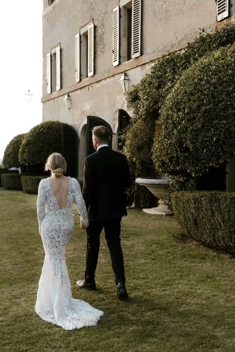 Bride and groom walking hand in hand beside the historic villa walls at Borgo Stomennano during golden hour.