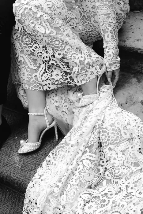 Bride adjusting her pearl heels, lace dress spilling around her on the stone steps at Borgo Stomennano
