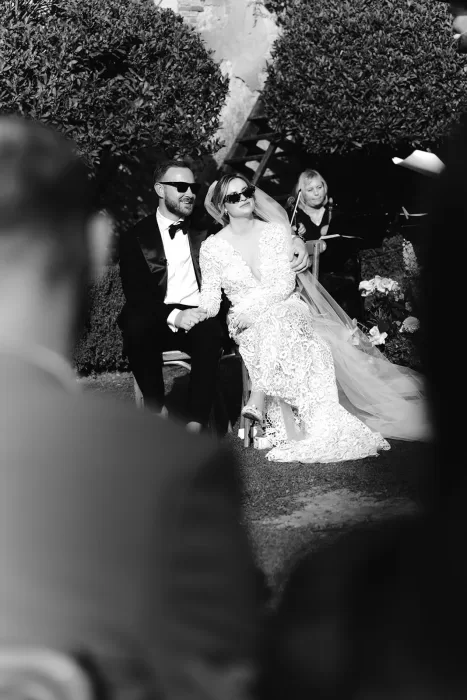Bride and groom holding hands and wearing sunglasses during their ceremony at Borgo Stomennano