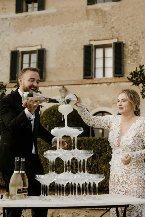 Bride and groom joyfully pouring champagne into a cascading tower at Borgo Stomennano
