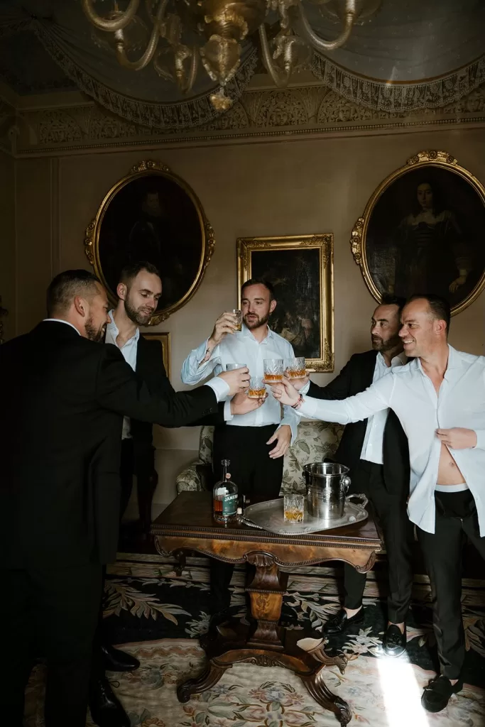 Groomsmen toasting with whiskey in an opulent room at Borgo Stomennano