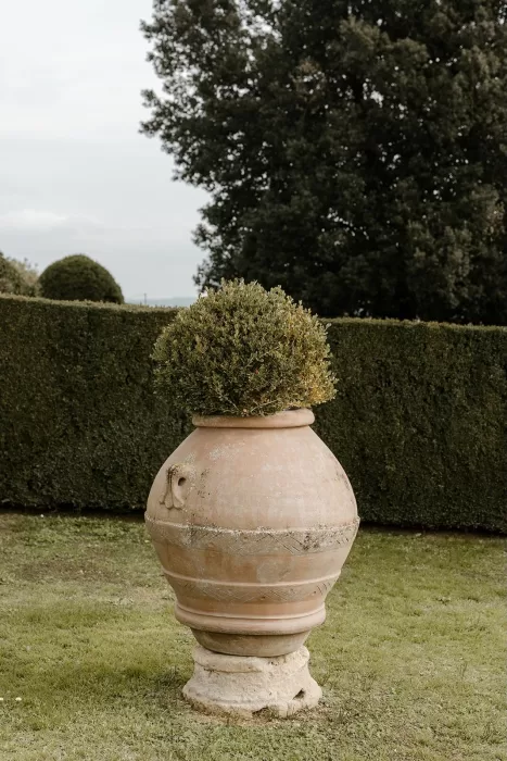 Large terracotta urn overflowing with greenery set against manicured hedges at Borgo Stomennano’s garden.