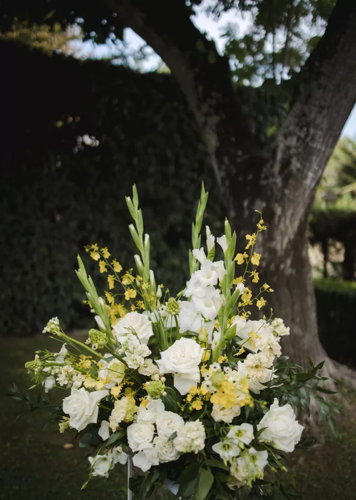 Lush arrangement of white and yellow wedding flowers under a tree at Borgo Tre Rose.