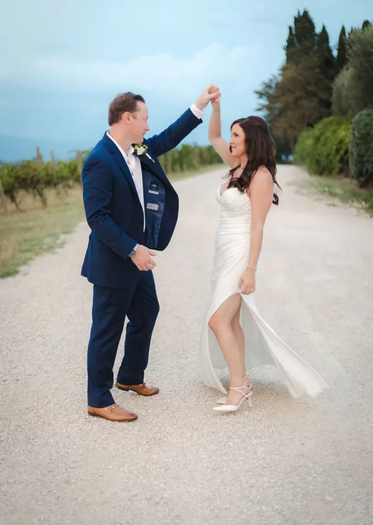Bride twirls in the groom's arms on a quiet road near the vineyards of Borgo Tre Rose.