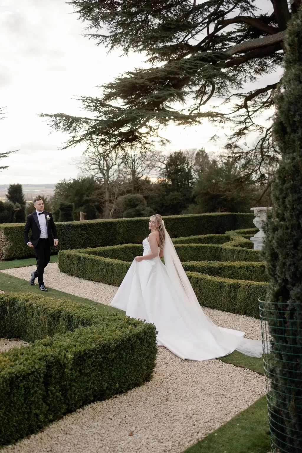 Bride and groom playfully explore manicured maze gardens on their wedding day, photographed by Sharon Cudworth