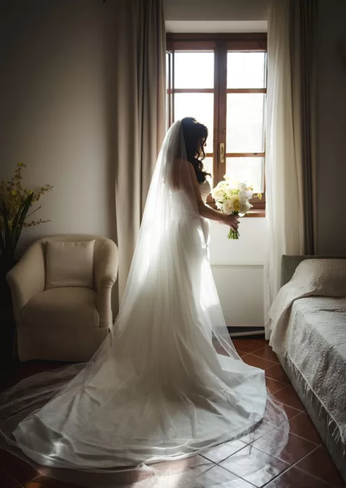 Bride standing by a sunlit window in her gown at Borgo Tre Rose