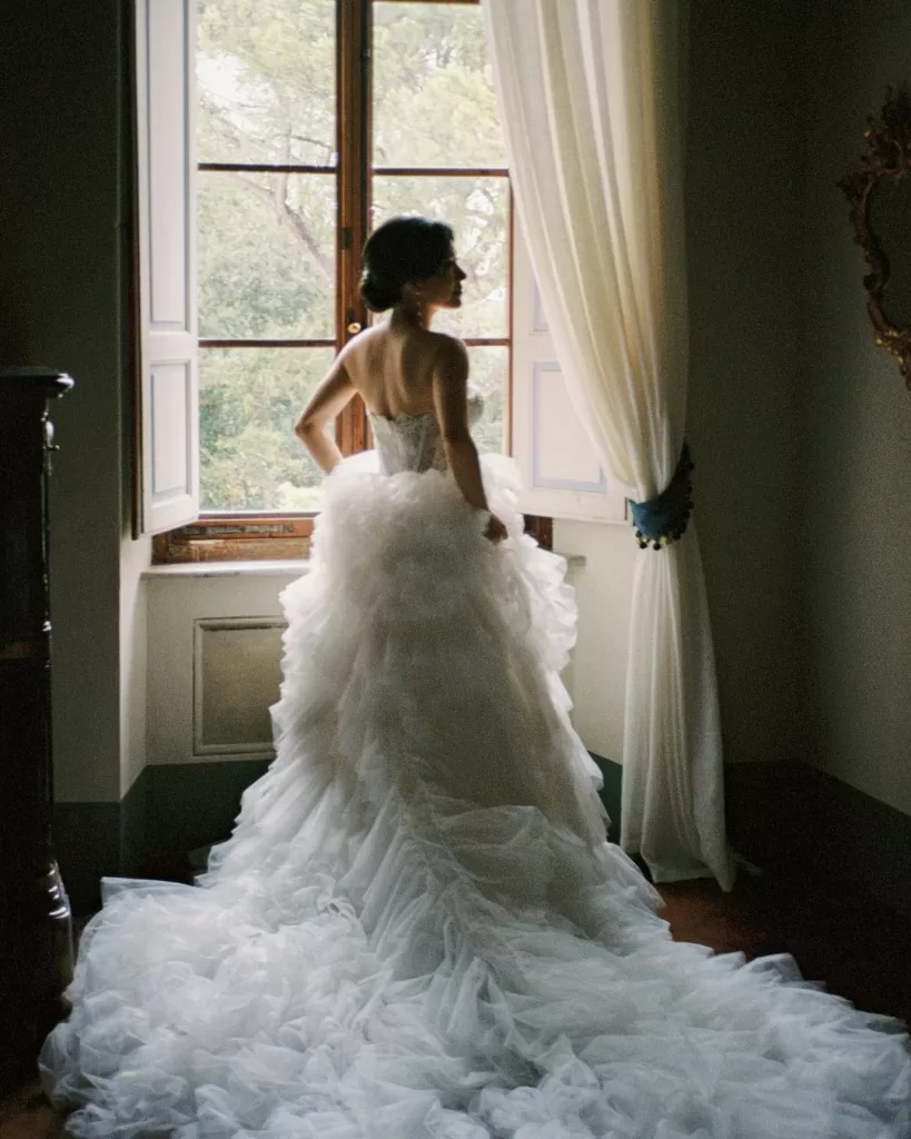The bride stands by the window, bathed in soft natural light, moments before the ceremony.