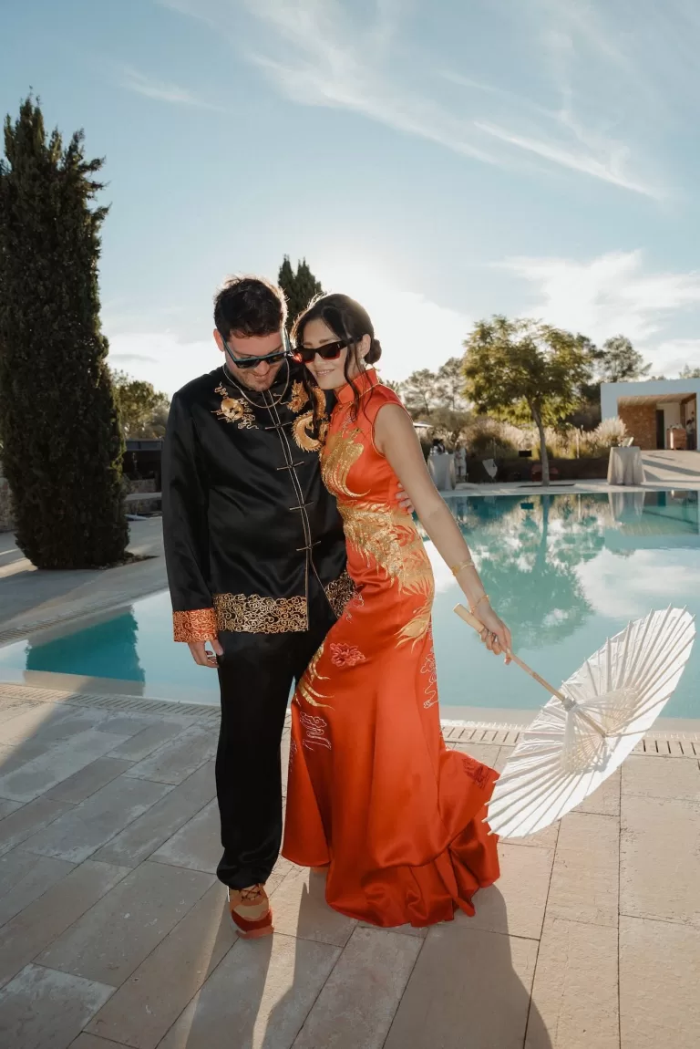 Bride and groom pose stylishly by the pool at Ca Na Xica, bride holding a white parasol in the sunshine.