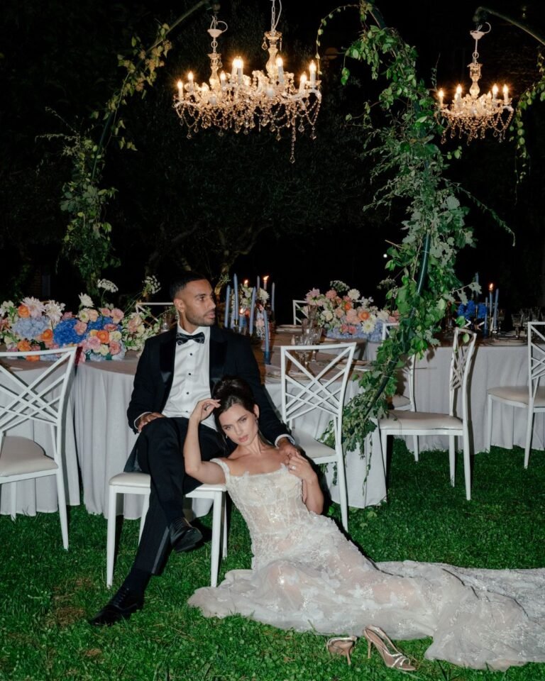 The couple shares a quiet moment under chandeliers at Castello Montignano, with the bride resting against the groom in her floral gown.