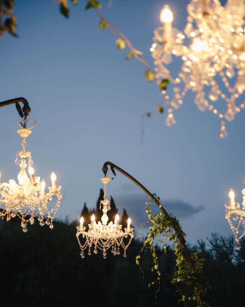 Crystal chandeliers suspended beneath twilight skies at Castello Montignano, adding sparkle to the garden celebration.