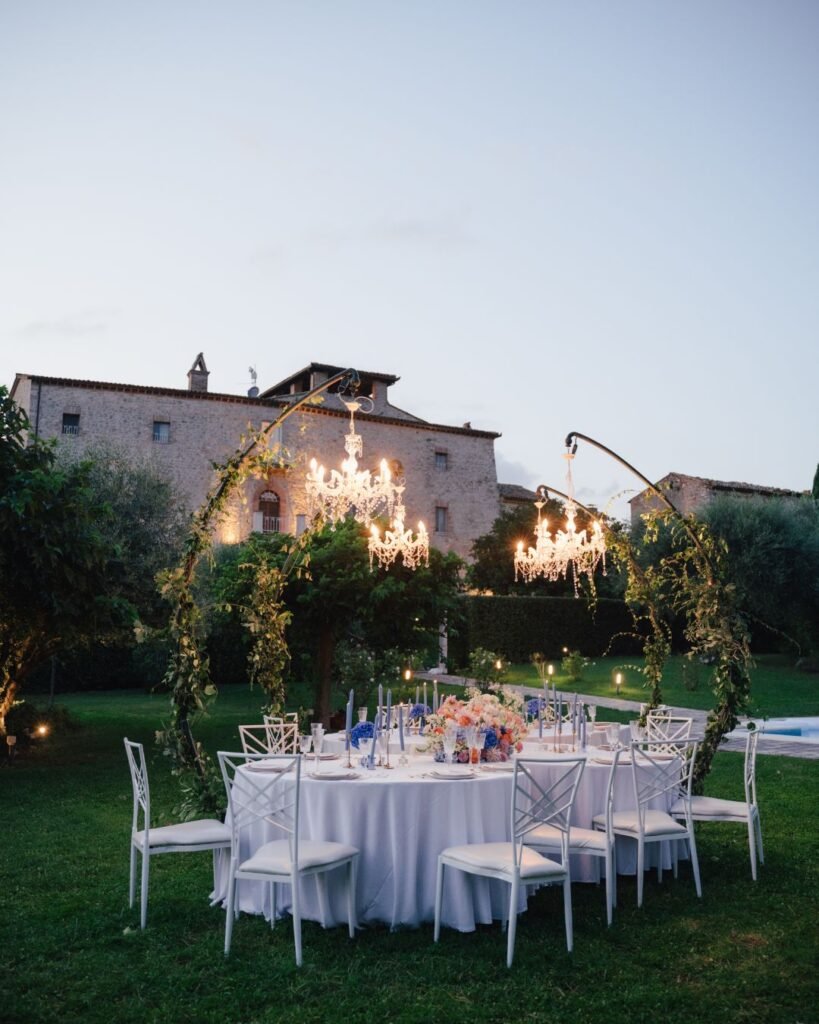 Castello Montignano wedding reception under crystal chandeliers as evening falls, surrounded by greenery and candlelight.