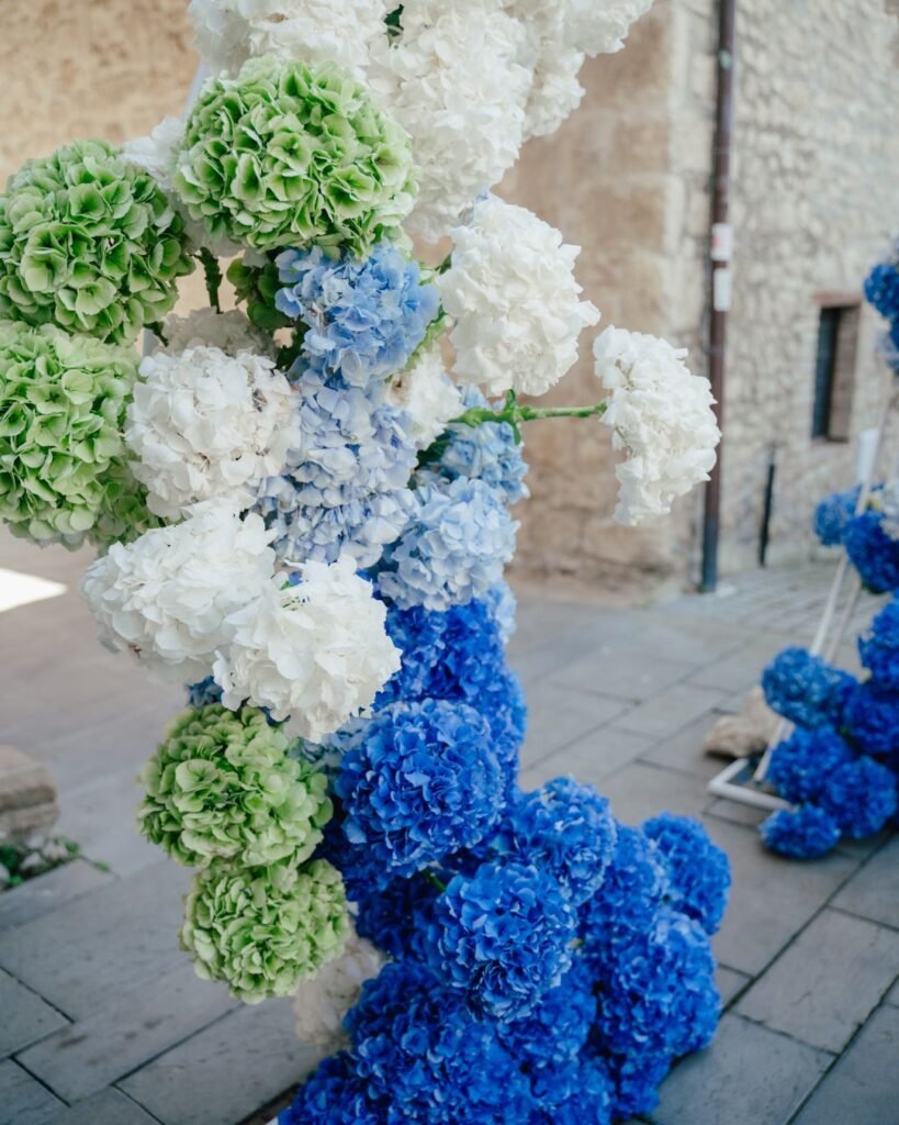 Close-up of vibrant blue, green, and white hydrangea floral arch in the stone courtyard of Castello Montignano.