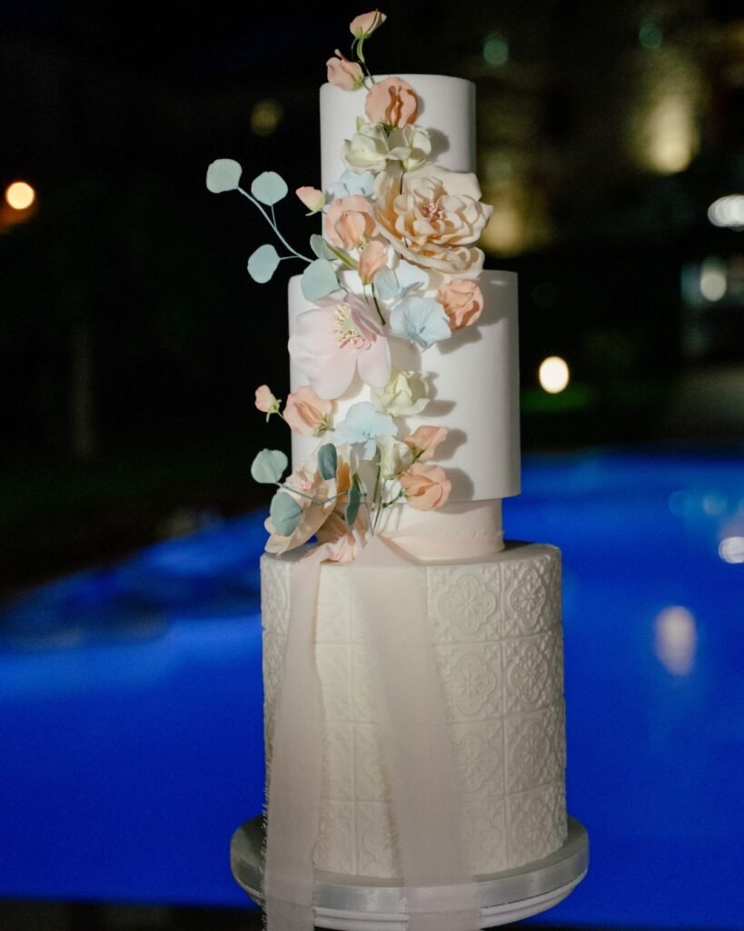 Three-tiered wedding cake with sugar flowers beside the pool at Castello Montignano, glowing in the evening light.