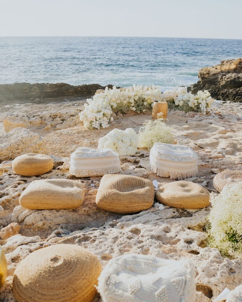 Cushioned floor seating arranged in a semi-circle on the rocky cliff edge for an intimate seaside ceremony.