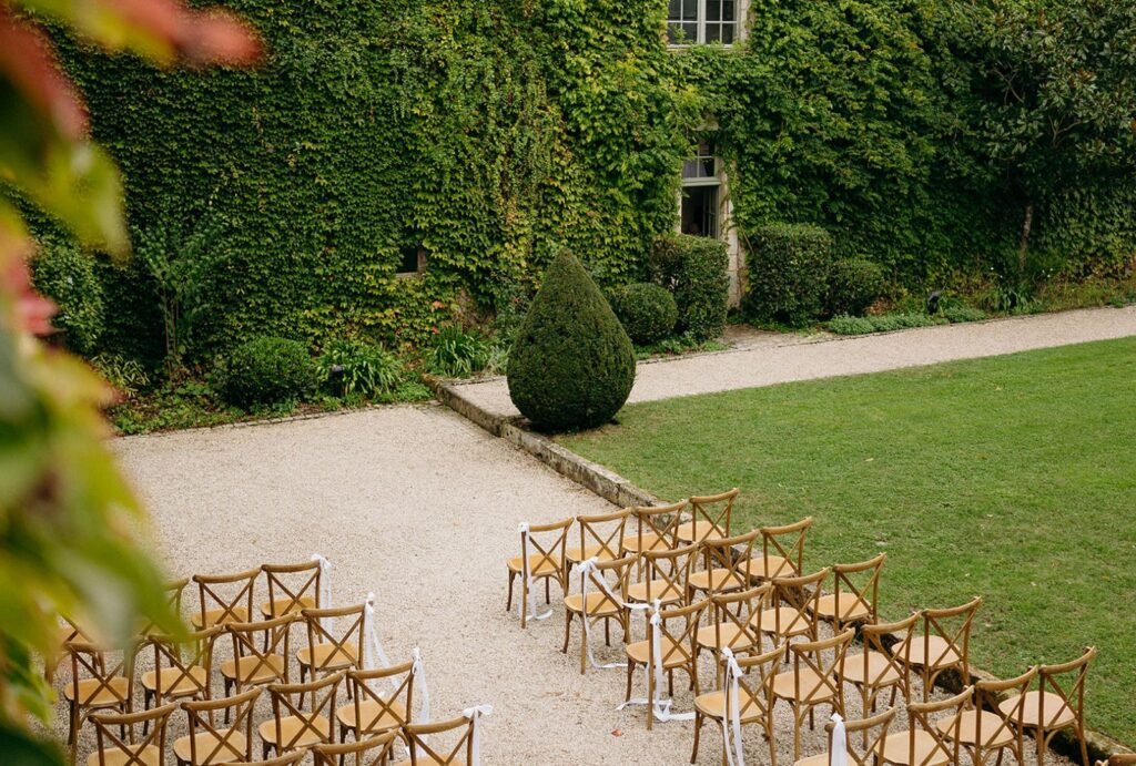 Wooden ceremony chairs with white ribbons set in the courtyard of Château Rigaud, surrounded by lush ivy-covered walls.