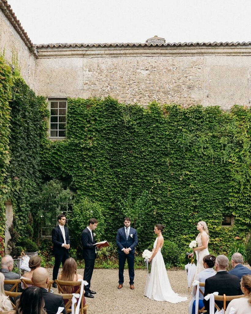 Wedding ceremony at Château Rigaud with ivy-covered walls as the backdrop and wooden chairs lining the gravel aisle.