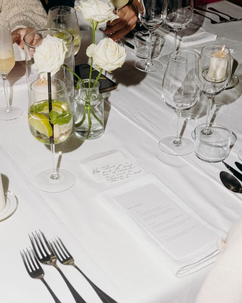 Elegant white table setting with roses, menus, and cocktails at Château Rigaud wedding reception.