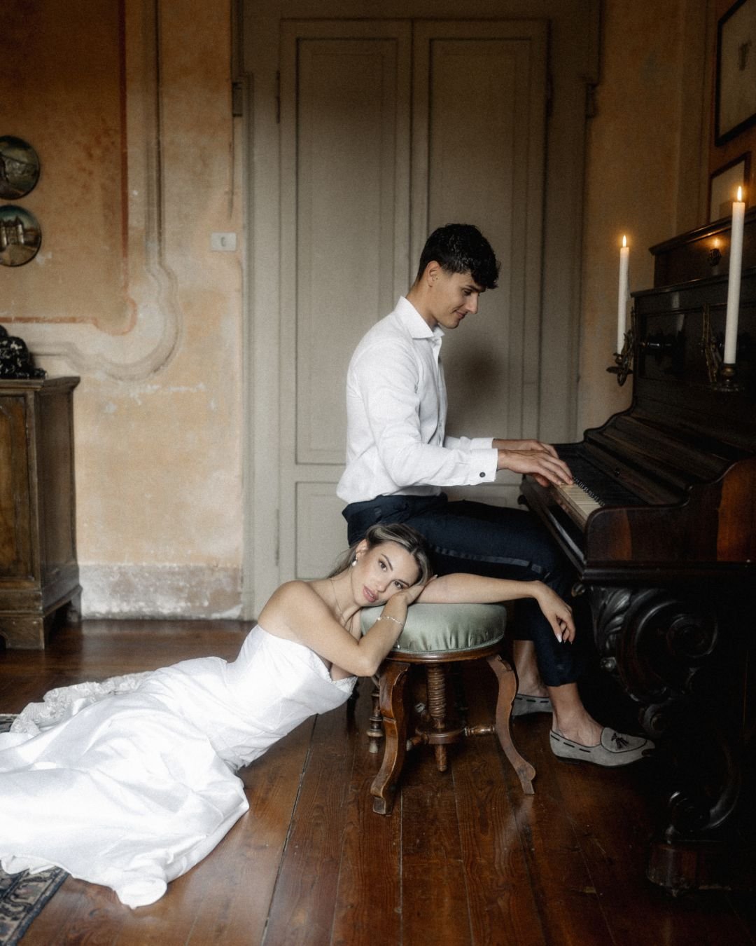 Romantic portrait of bride resting beside groom playing piano in historic villa setting, photographed by Lukas Hanifle.