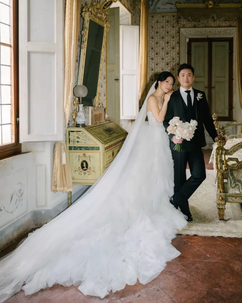 The bride and groom share an intimate moment in a vintage-style room, bathed in soft light.
