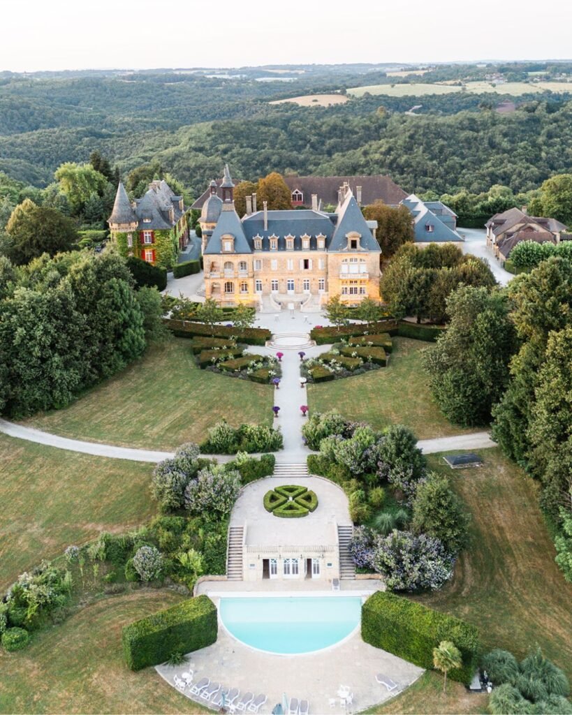 Captivating aerial perspective highlighting Domaine d'Essendiéras' grand château, formal gardens, and serene swimming pool.