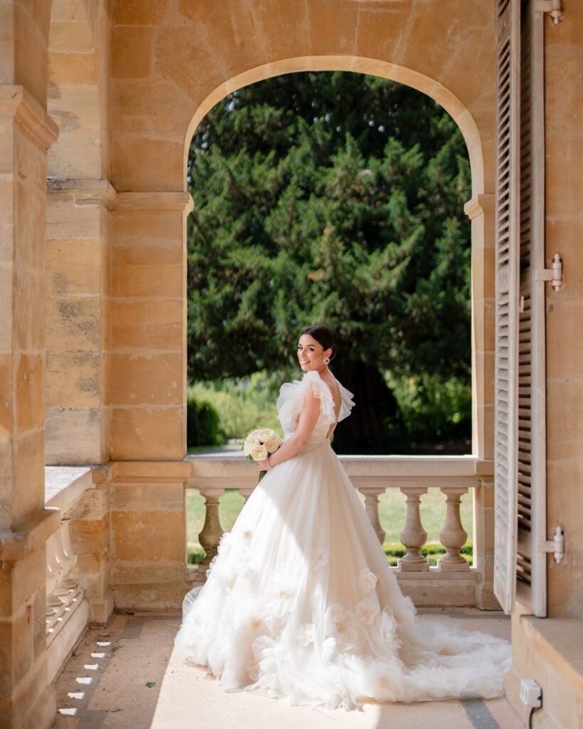Graceful bride holding bouquet, framed by elegant stone arches at Domaine d'Essendiéras.