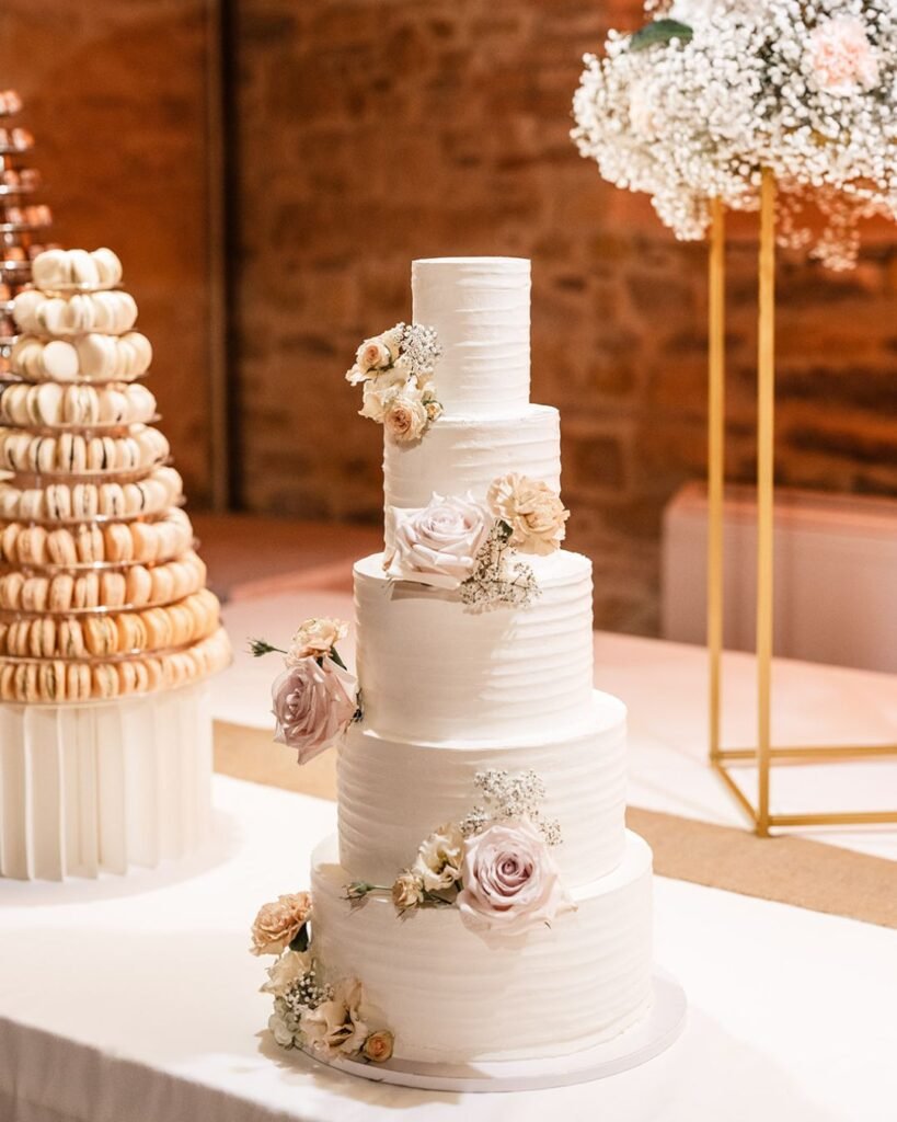 Elegant tiered wedding cake adorned with delicate pastel roses, displayed beside a sophisticated macaron tower at Domaine d'Essendiéras.