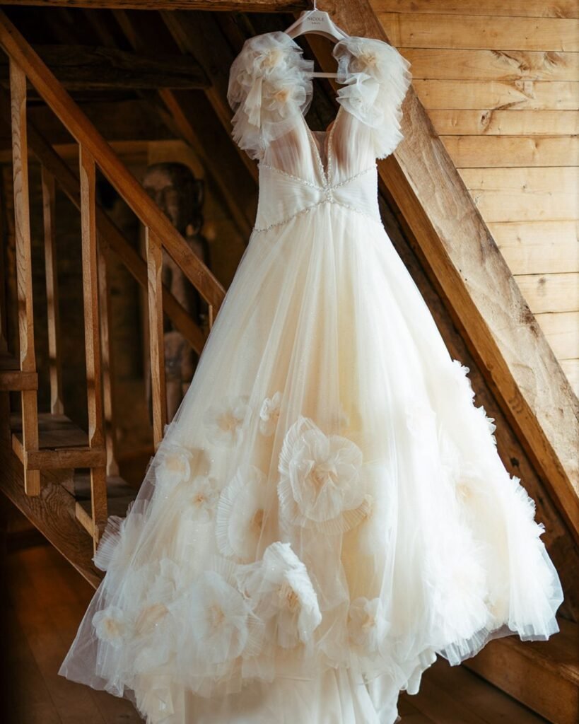 Elegant floral-embroidered wedding dress hanging in rustic wooden interior at Domaine d'Essendiéras.