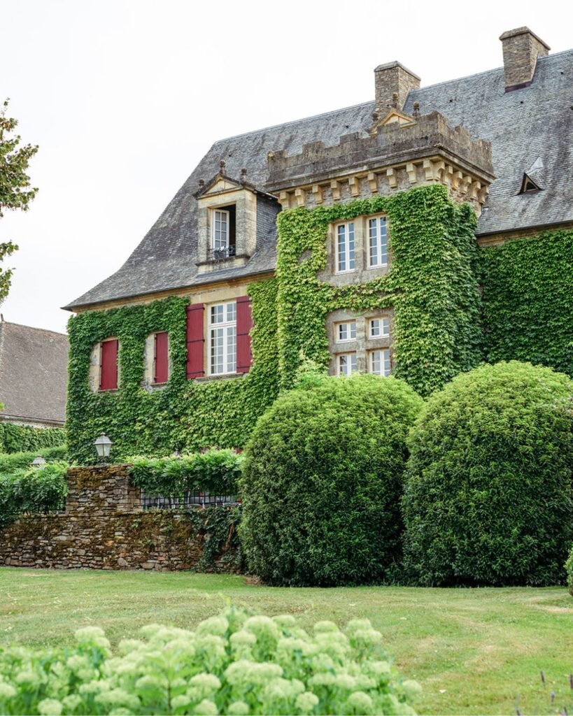 Picturesque Domaine d'Essendiéras building draped in lush ivy, with red shutters enhancing its rustic charm.